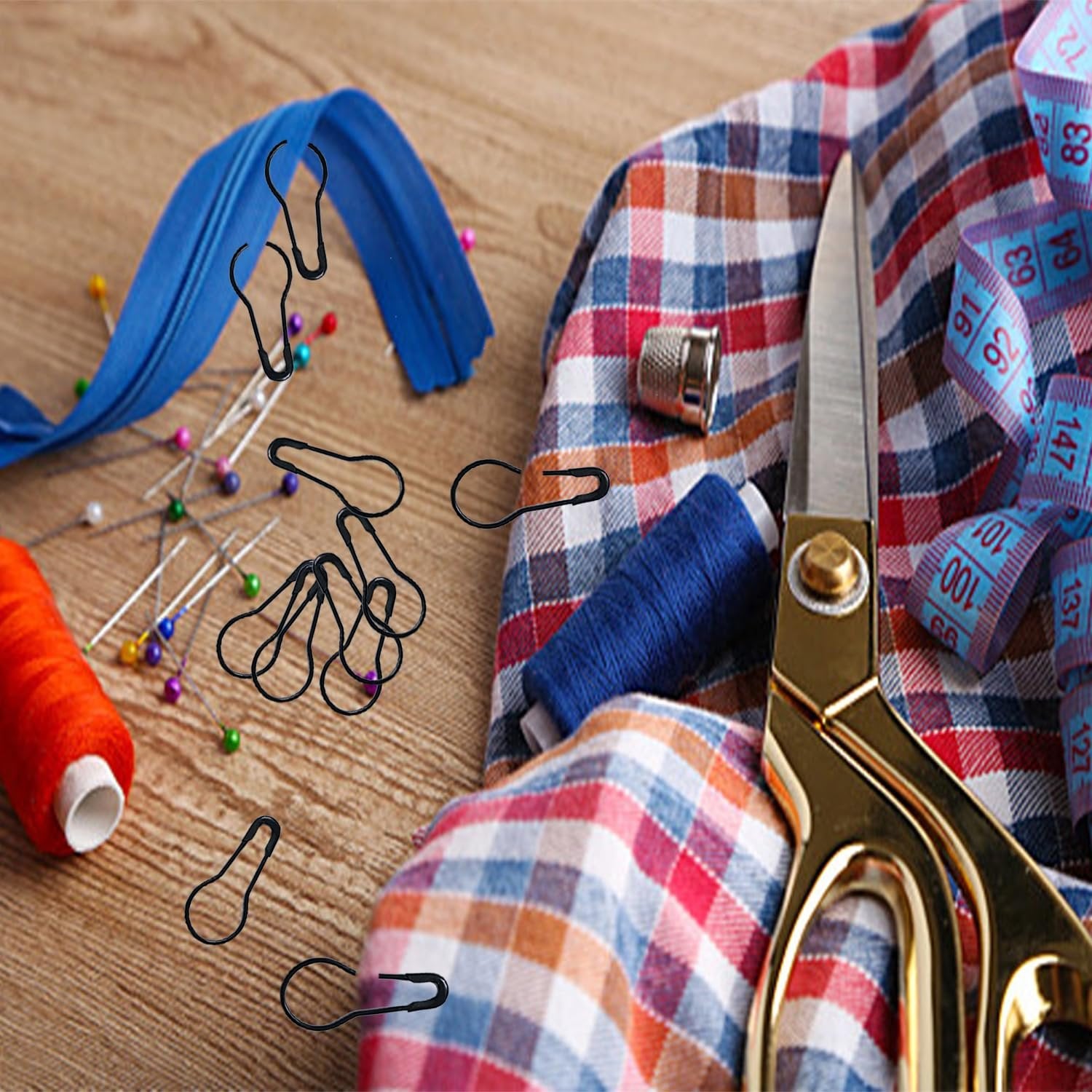 Black metal bulb safety pins scattered with sewing supplies including a blue zipper, thread, scissors, and measuring tape on a wooden surface.