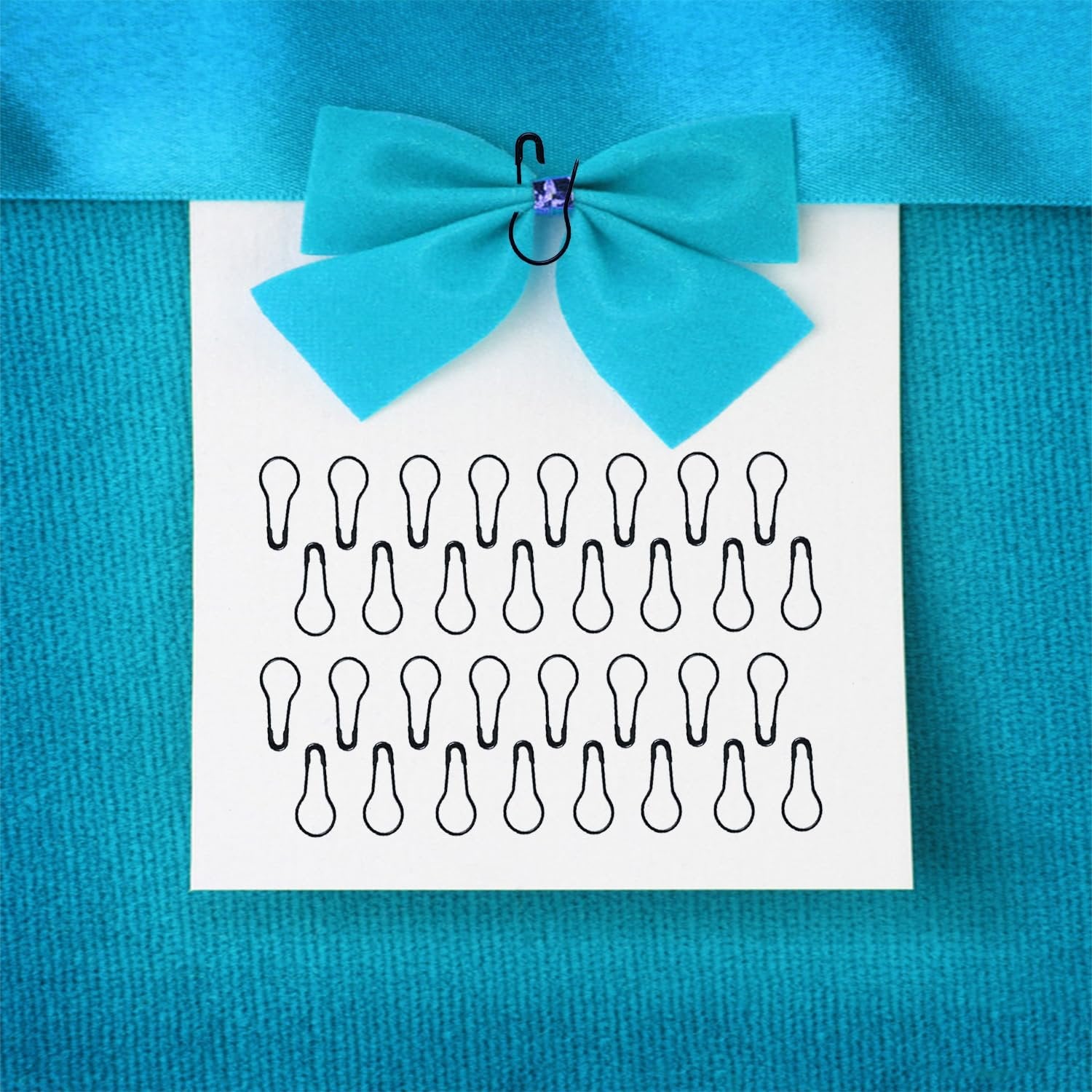 Black gourd-shaped safety pins displayed on a white card with a blue bow and ribbon against a textured blue background.