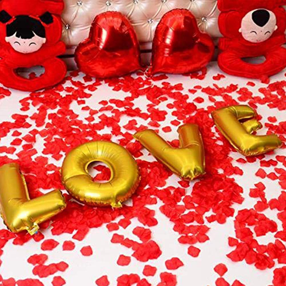 Gold 'LOVE' balloons scattered on red artificial rose petals with plush red characters and heart balloons in background