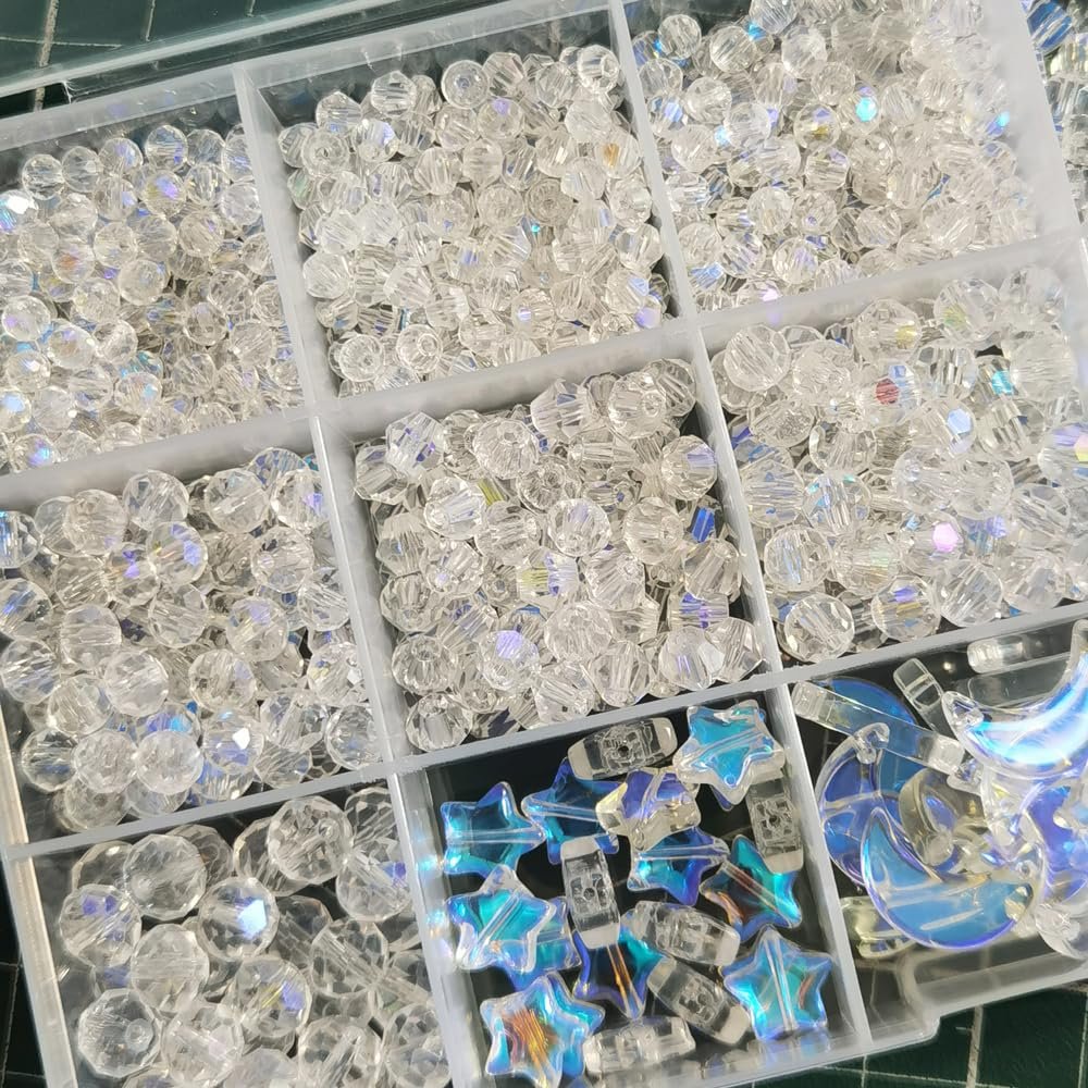 Assorted clear crystal glass beads in various shapes and sizes, including round, star, and crescent moon, organized in a compartmentalized tray.