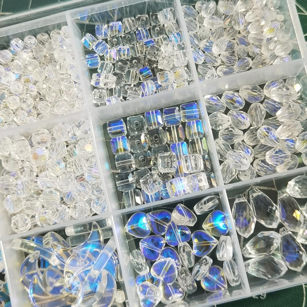Assorted clear and iridescent crystal glass beads in various shapes and sizes, organized in a compartmentalized tray for jewelry making.