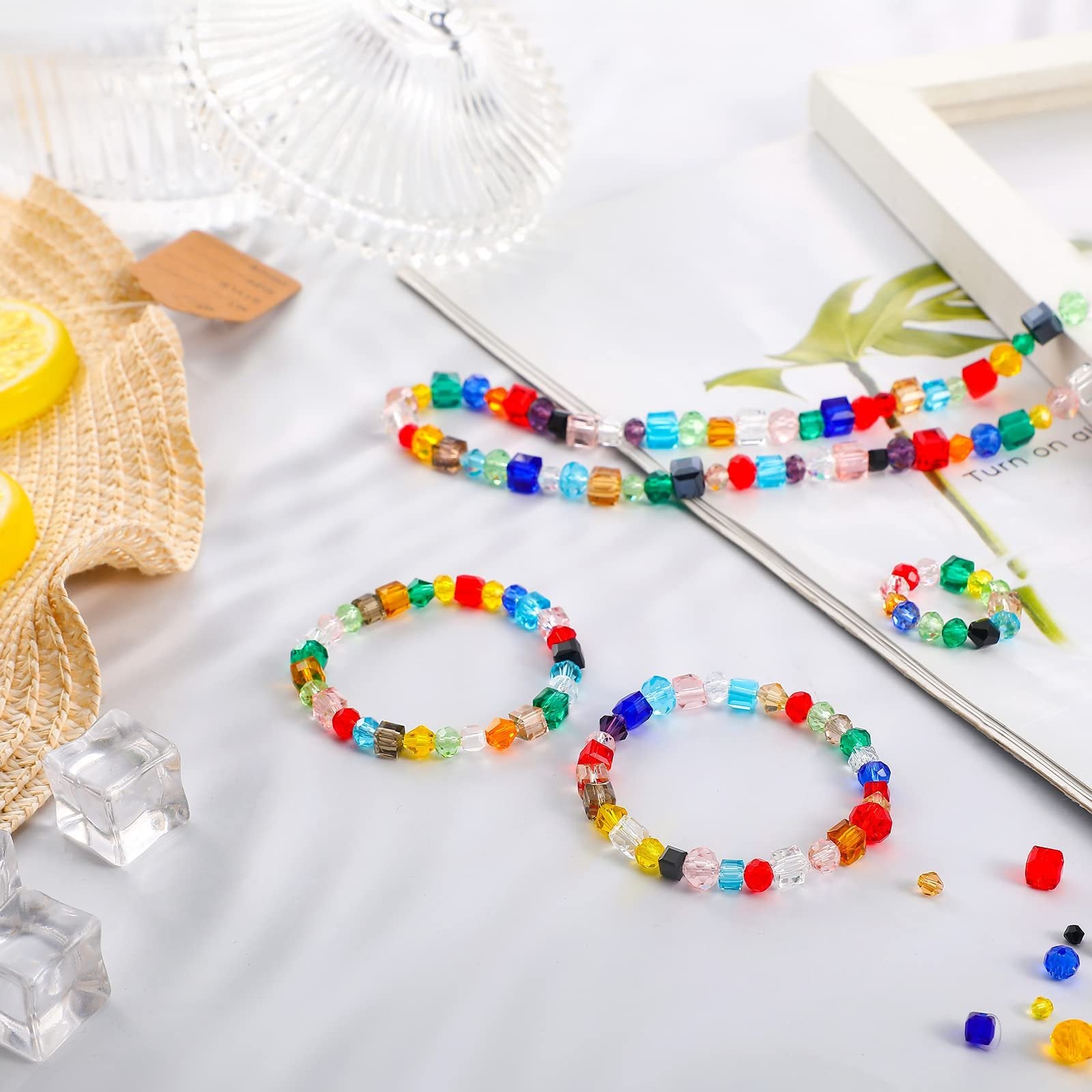 Assorted colorful faceted glass beads arranged into bracelets and a necklace on a white surface with decorative elements.