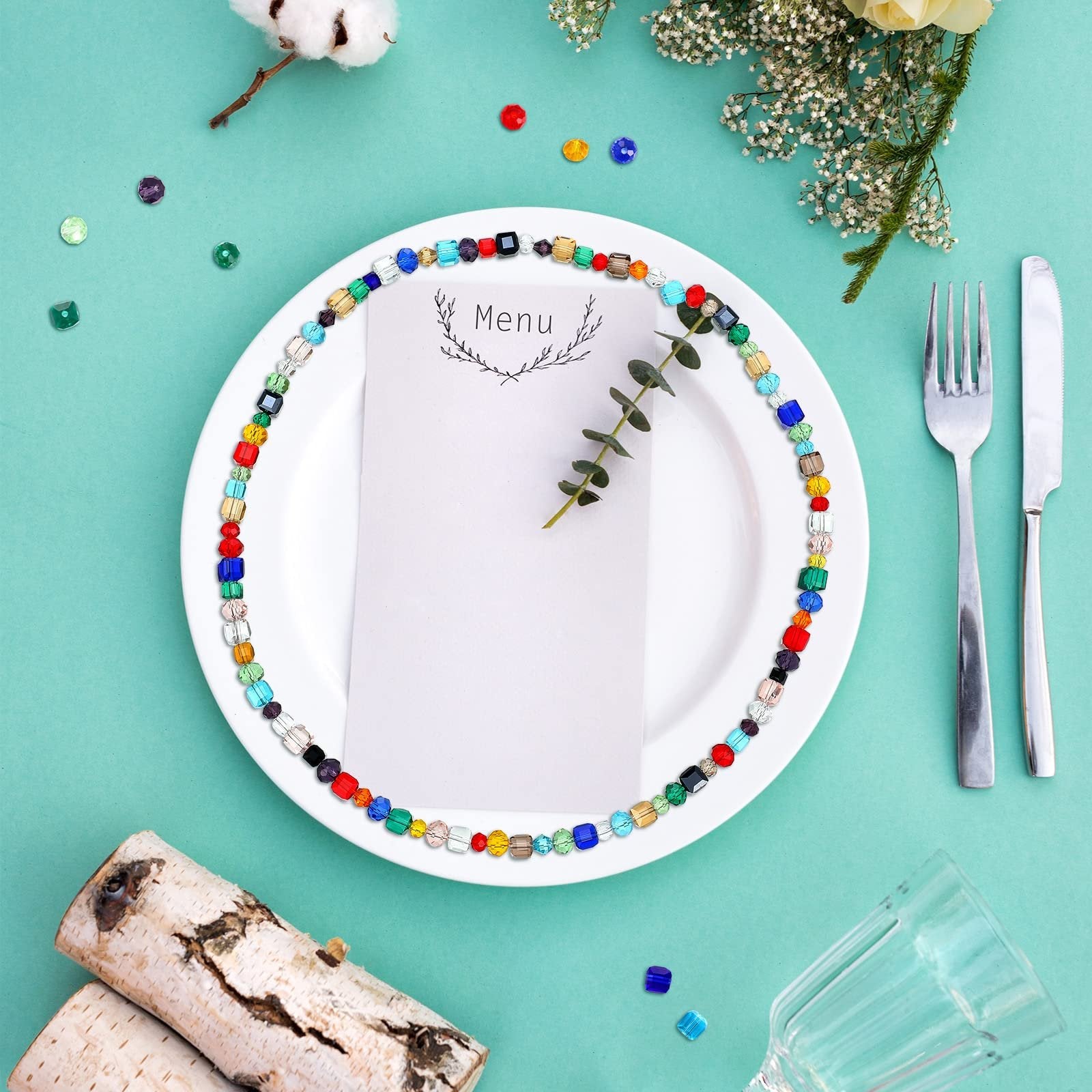 Table setting with a white plate adorned with colorful faceted glass beads, a menu card, cutlery, and decorative elements.