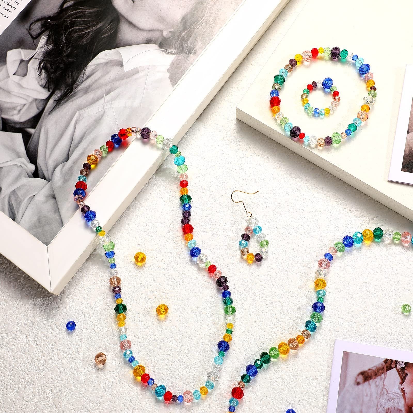 Assortment of colorful faceted crystal beads arranged as a necklace, bracelet, and earring on a white textured surface with a black and white photo in the background.