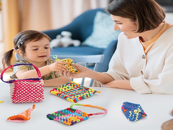 Mother and daughter weaving colorful crafts on a white table, with finished woven items scattered around.