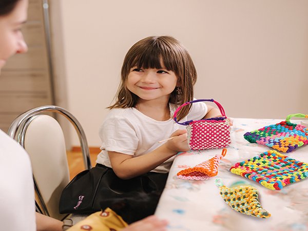 Smiling young girl weaving colorful crafts at a table with an adult