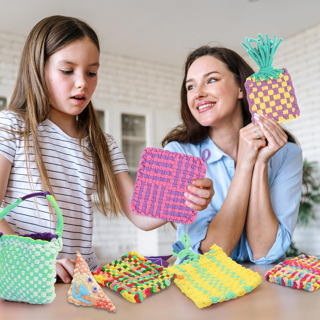 Woman and girl holding colorful woven crafts made with loom loops, with more crafts on table.