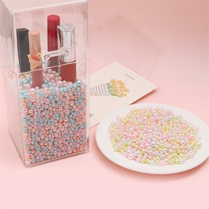 Clear container filled with mixed size pastel no-hole pearls and lipsticks, next to a plate of pearls and a floral card.