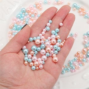 Hand holding a mix of small pink, blue, and peach no-hole craft pearls in various sizes.