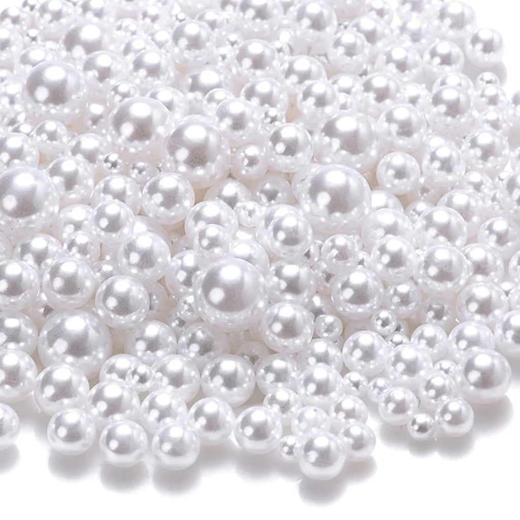 Pile of mixed-size white no-hole ABS plastic craft pearls on a white background.