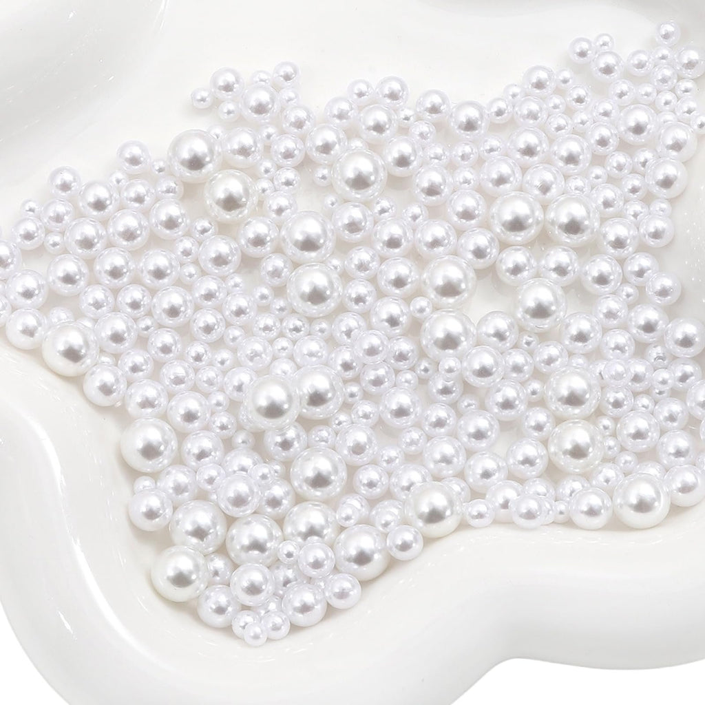 Close-up overhead view of mixed-size white no-hole pearls scattered on a white wavy surface.
