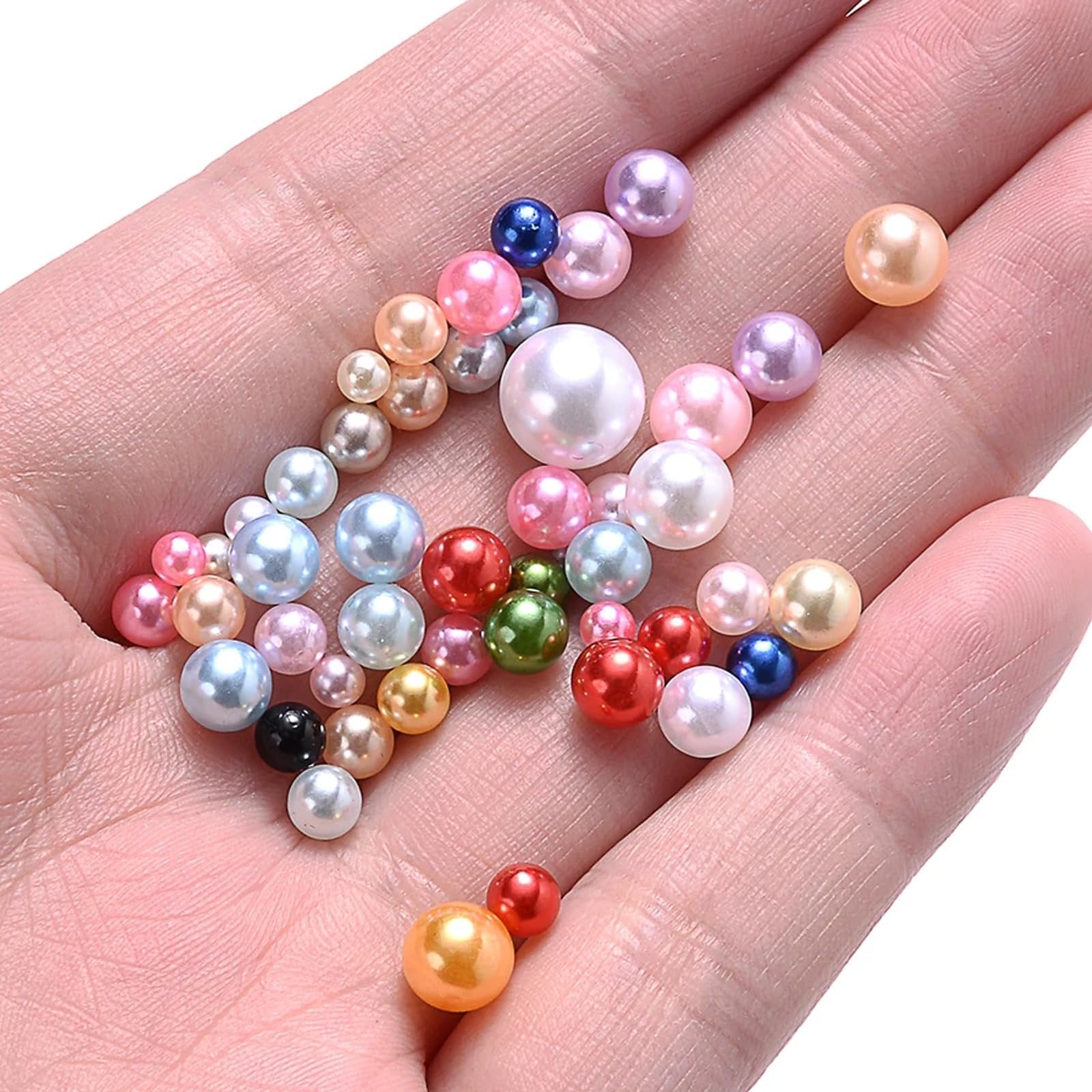 Hand holding a collection of mixed-size, multi-colored no-hole pearls for crafts.