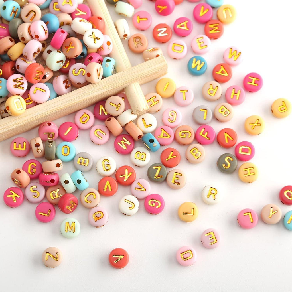 Colorful round acrylic letter beads with gold letters scattered and in a wooden tray, close-up view.