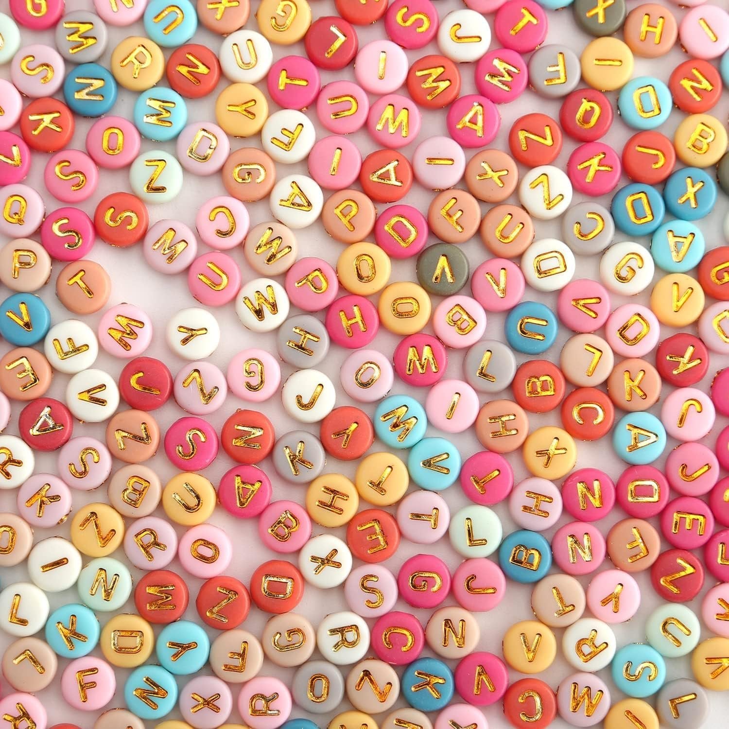 Colorful round acrylic alphabet beads with gold letters, scattered on a white surface.