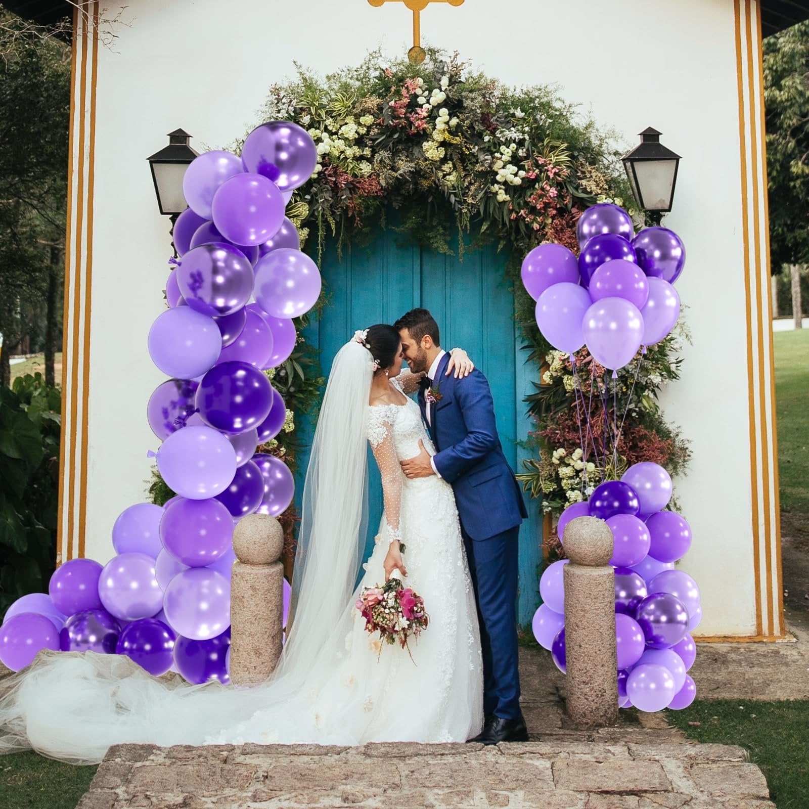 Bride and groom embracing in front of a floral archway decorated with purple balloons.