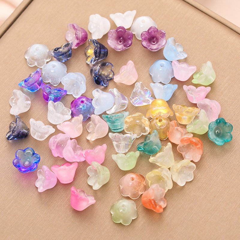 Assortment of colorful glass bellflower trumpet beads scattered on a textured surface.