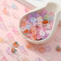 Assorted colorful glass flower-shaped beads scattered on a pink surface and in a white dish.