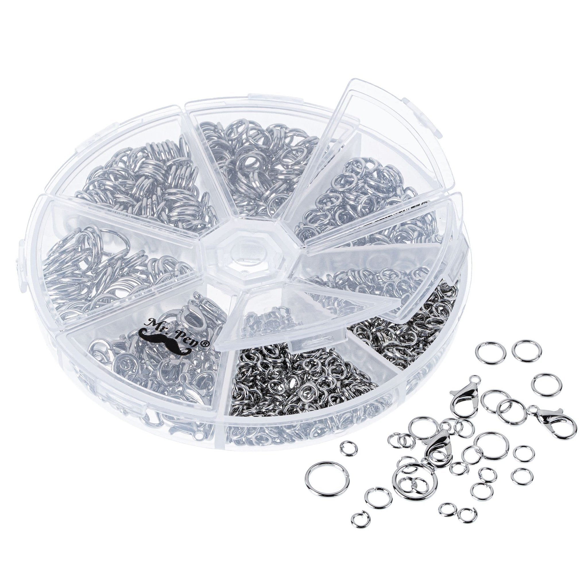 Open jump rings and lobster clasps in a clear divided organizer case, with some scattered outside.