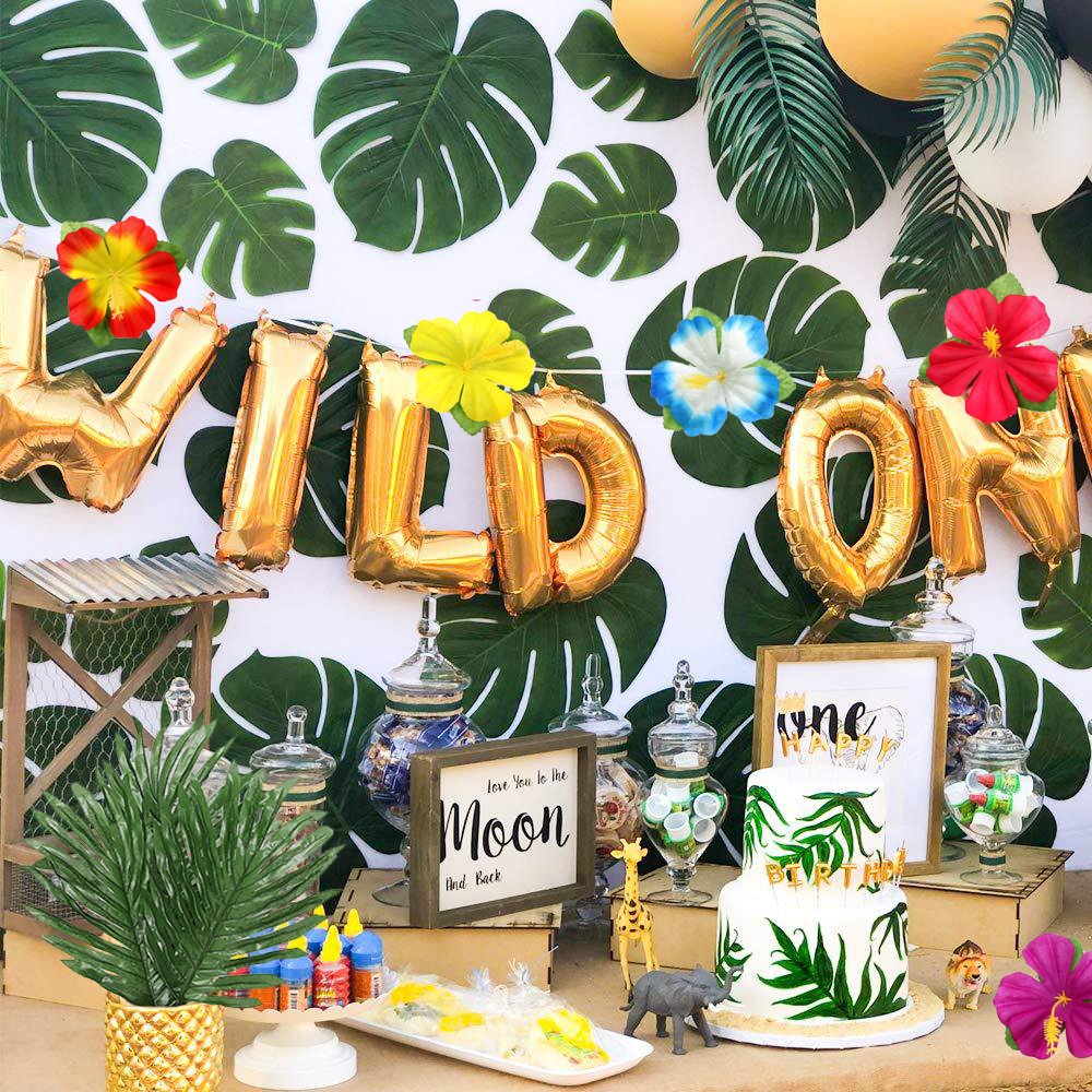 Tropical party setup with gold 'WILD ONE' balloons, cake, and jungle-themed decorations.