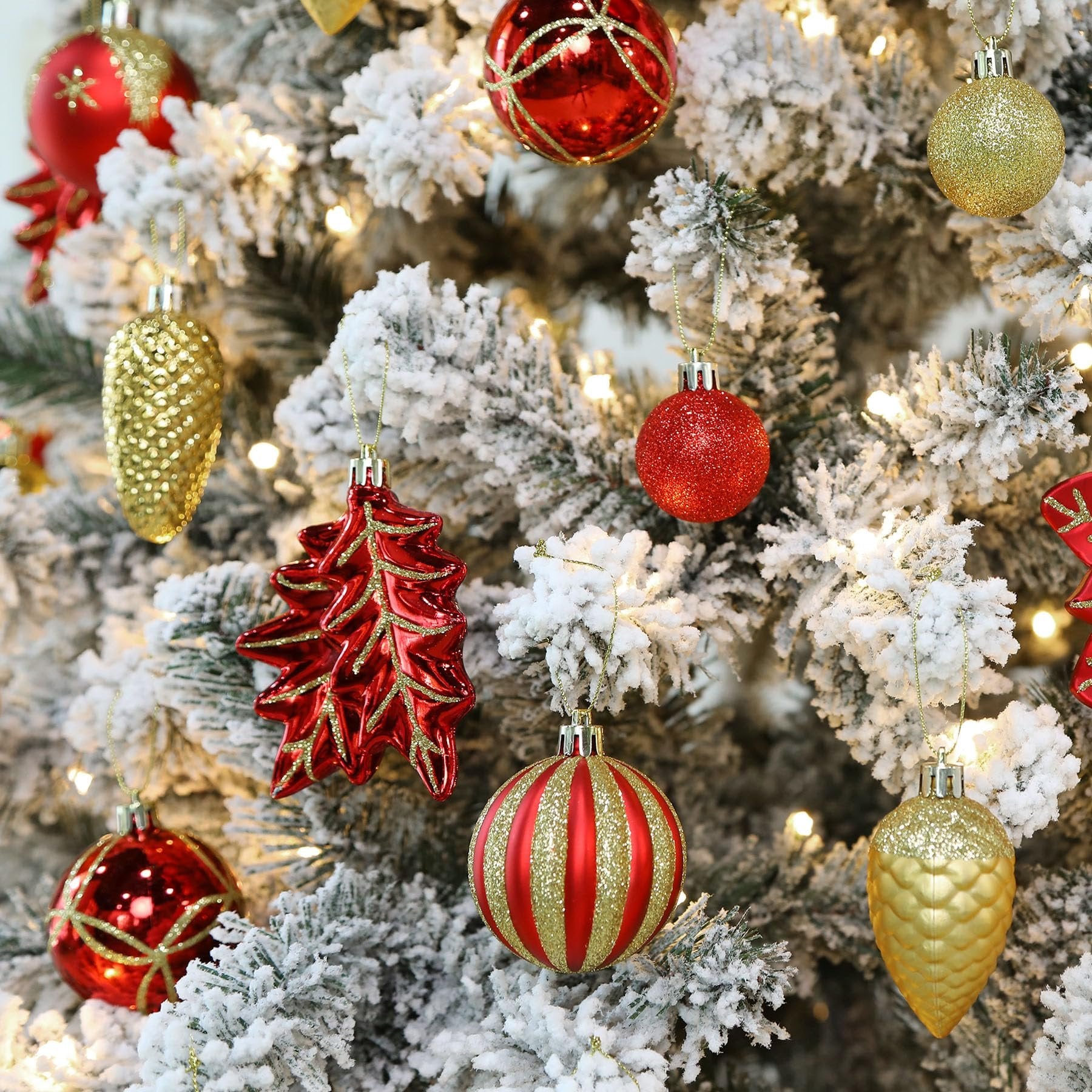 Assortment of red and gold Christmas ornaments hanging on a flocked tree with lights