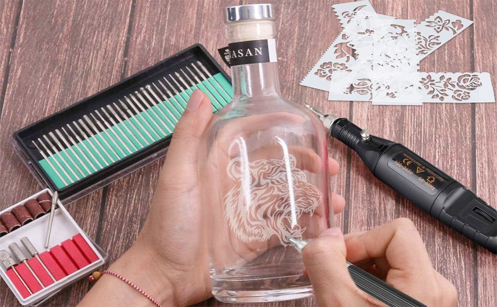 Person engraving a tiger design onto a glass bottle with a rotary tool kit and stencils.