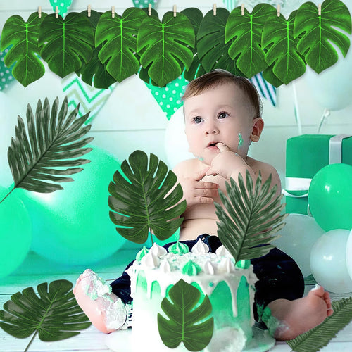 Baby sitting in front of a cake with artificial tropical leaves and balloons, celebrating a birthday.