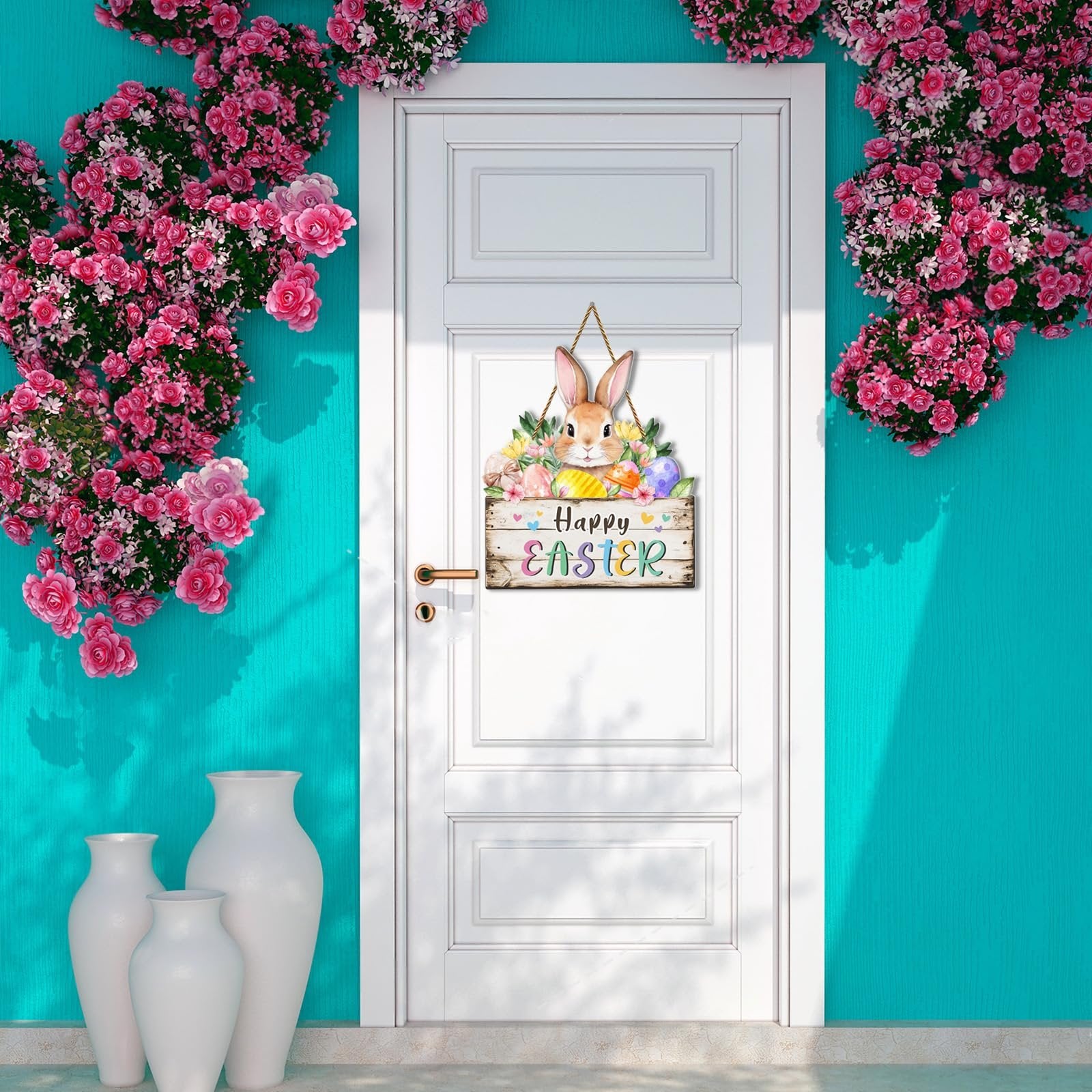 Easter door sign with bunny, eggs, and flowers hanging on a white door, flanked by pink floral arrangements.