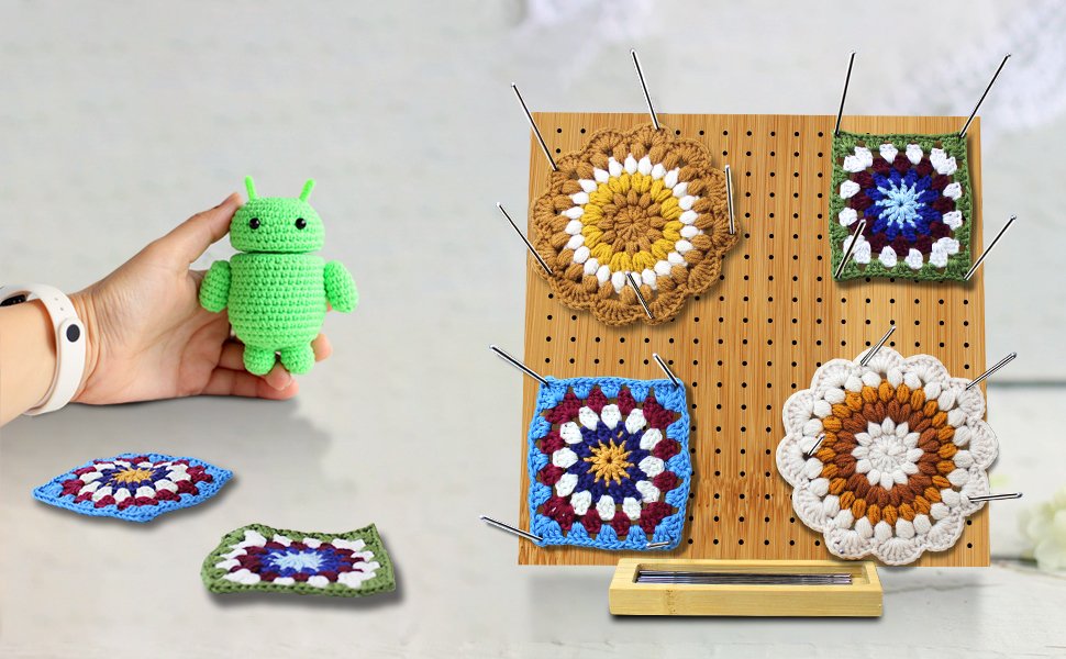 Bamboo blocking board with crochet granny squares pinned, and a hand holding a green crochet robot.