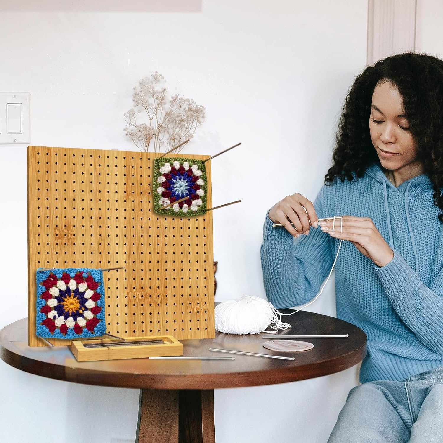 Woman crocheting with a bamboo blocking board and steel pins, featuring two finished granny squares.