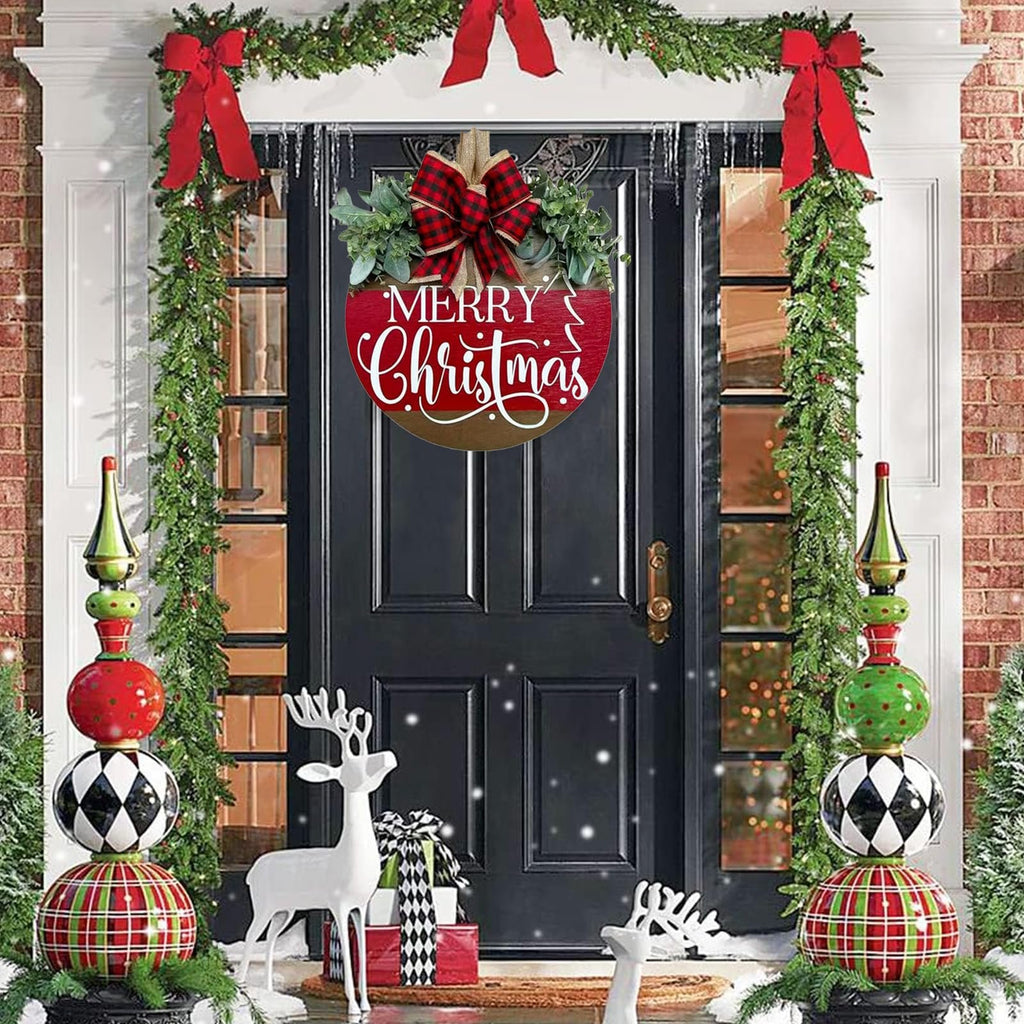 Round wooden Merry Christmas sign with red buffalo plaid bow and green eucalyptus leaves hanging on a black door decorated with Christmas garlands.