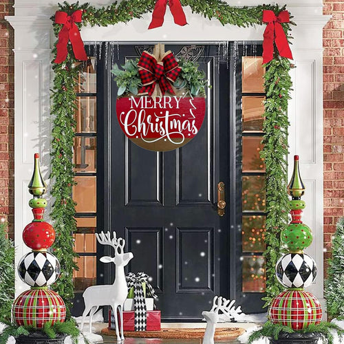 Round wooden Merry Christmas sign with red buffalo plaid bow and green eucalyptus leaves hanging on a black door decorated with Christmas garlands.
