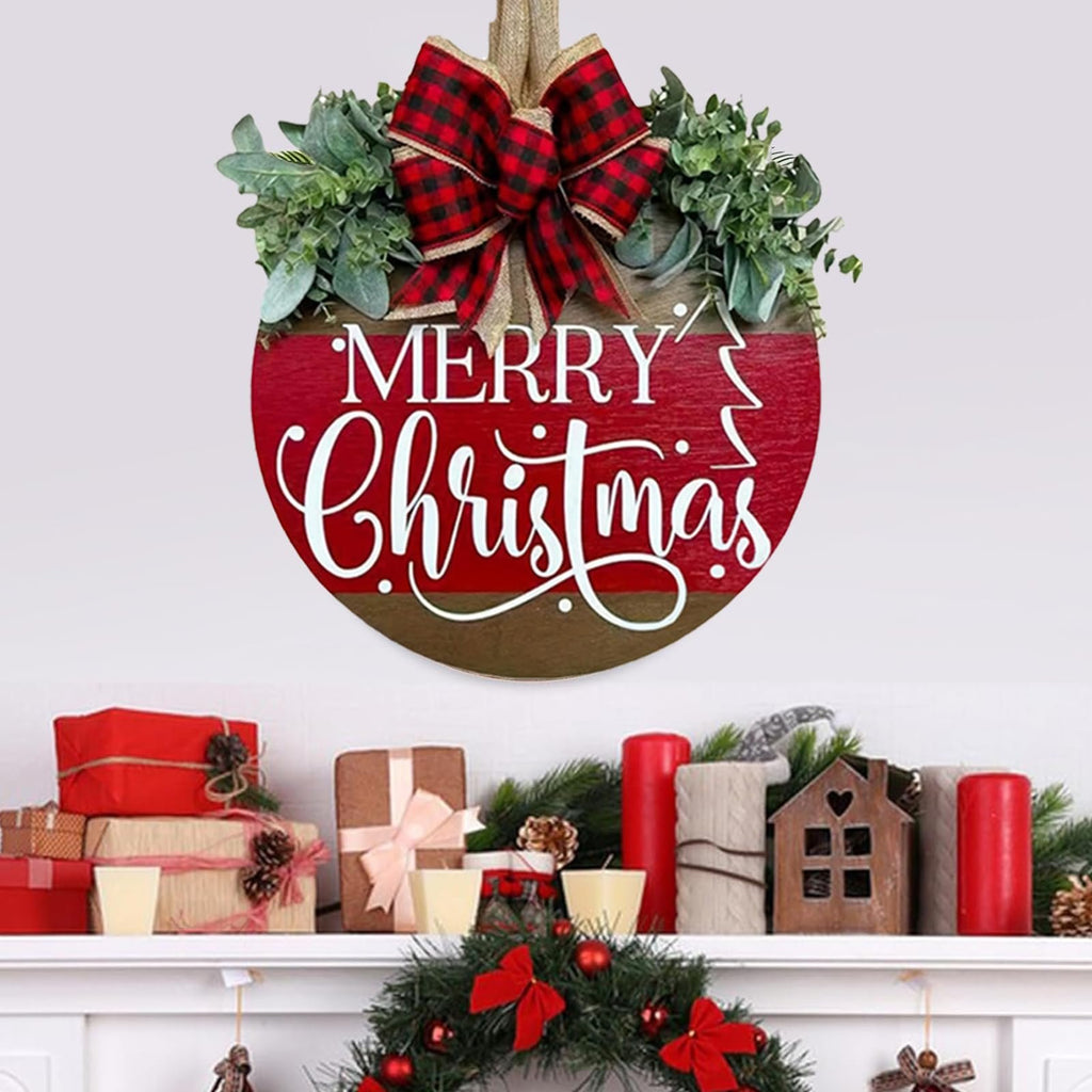 Round wooden Merry Christmas sign with red and white lettering, decorated with a plaid bow and green eucalyptus leaves, displayed above a mantelpiece with gifts and candles.