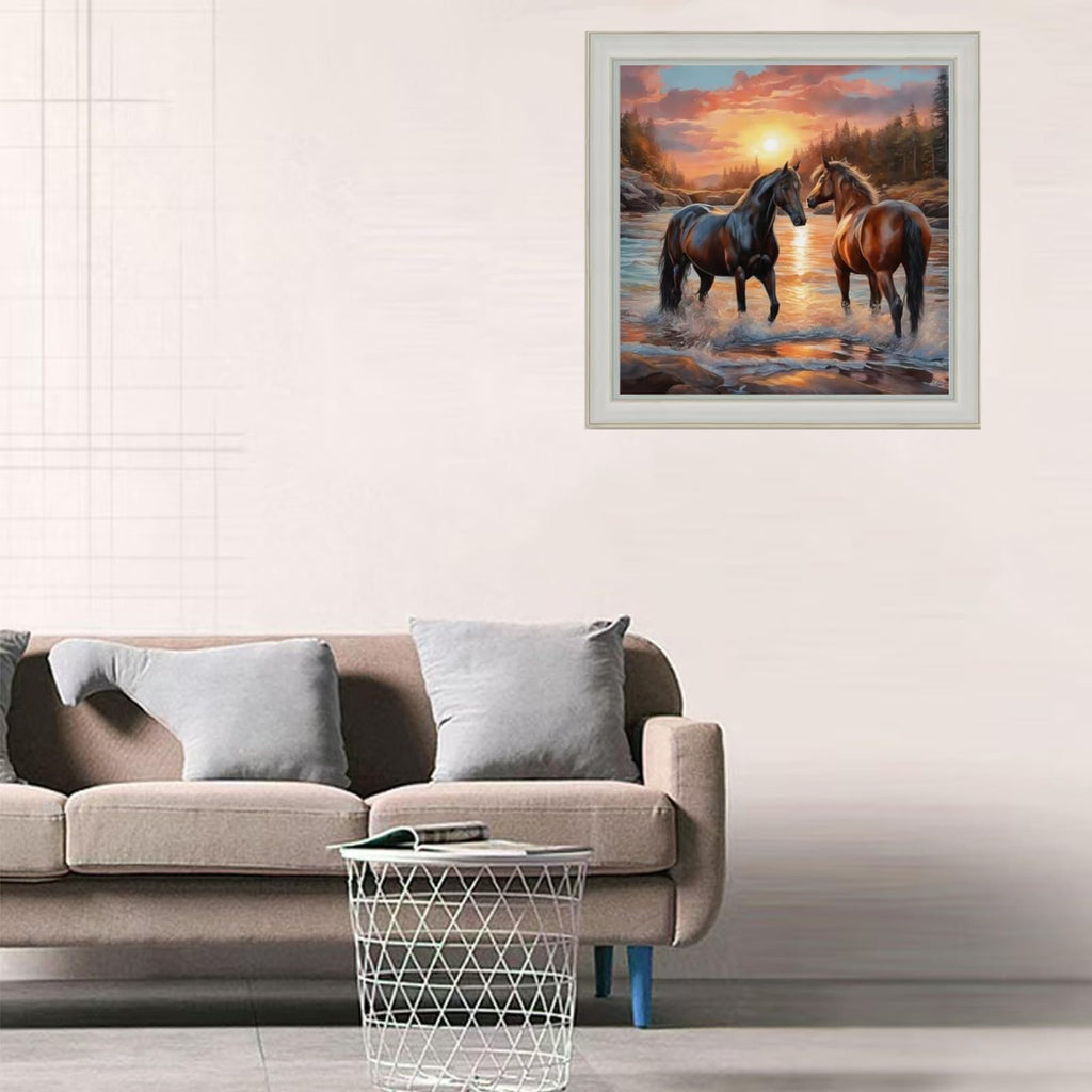 Diamond art painting of two horses in a river at sunset, framed and displayed on a wall above a sofa.