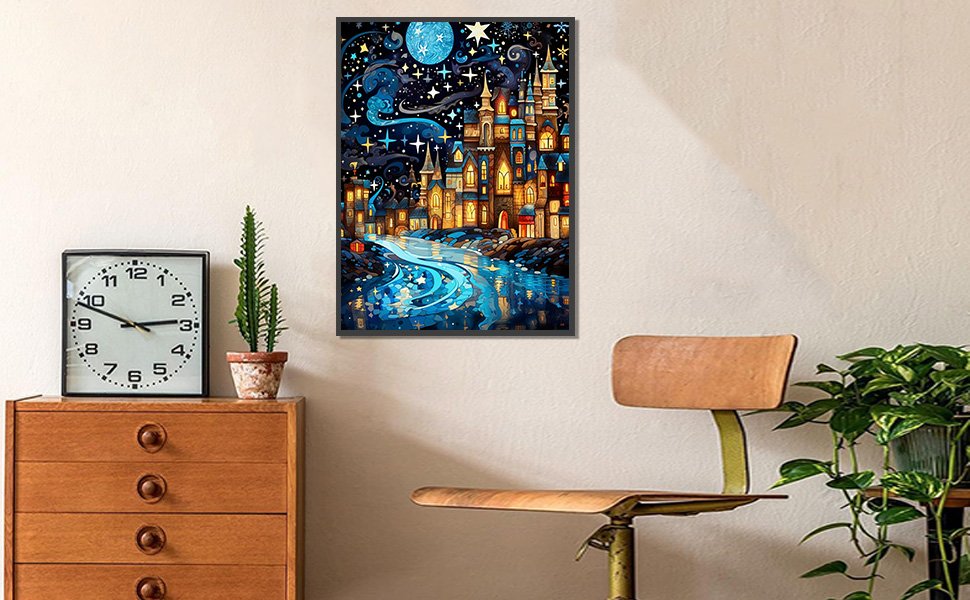Diamond painting kit of a starry night cityscape with a glowing river, framed and hung on a wall.