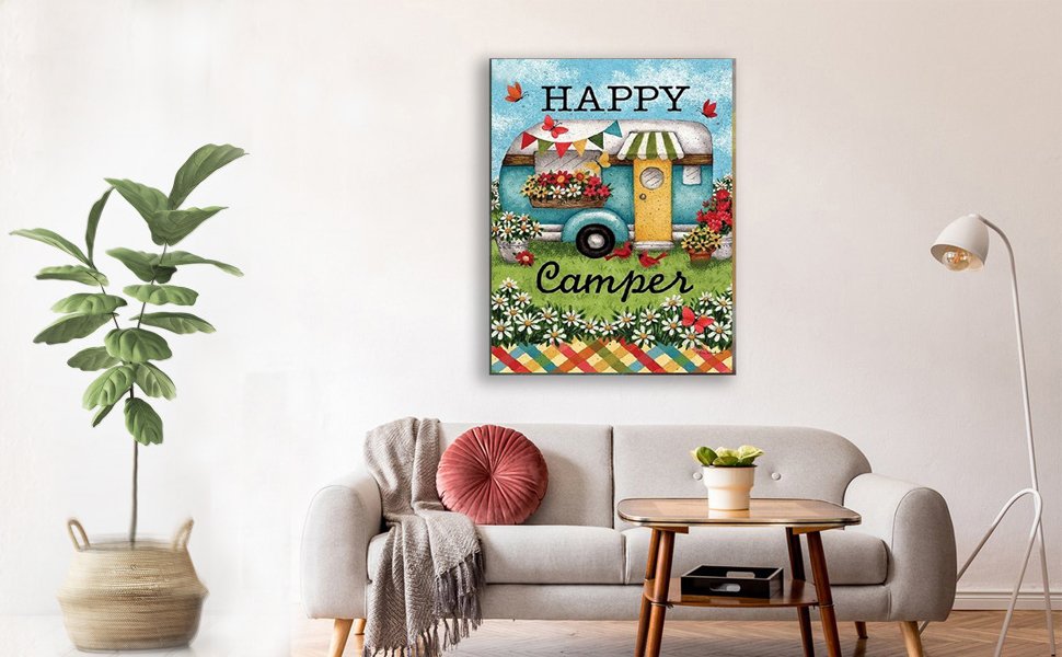 Diamond painting of a blue camper van with flowers and butterflies, text reads HAPPY CAMPER, displayed on a wall above a sofa.