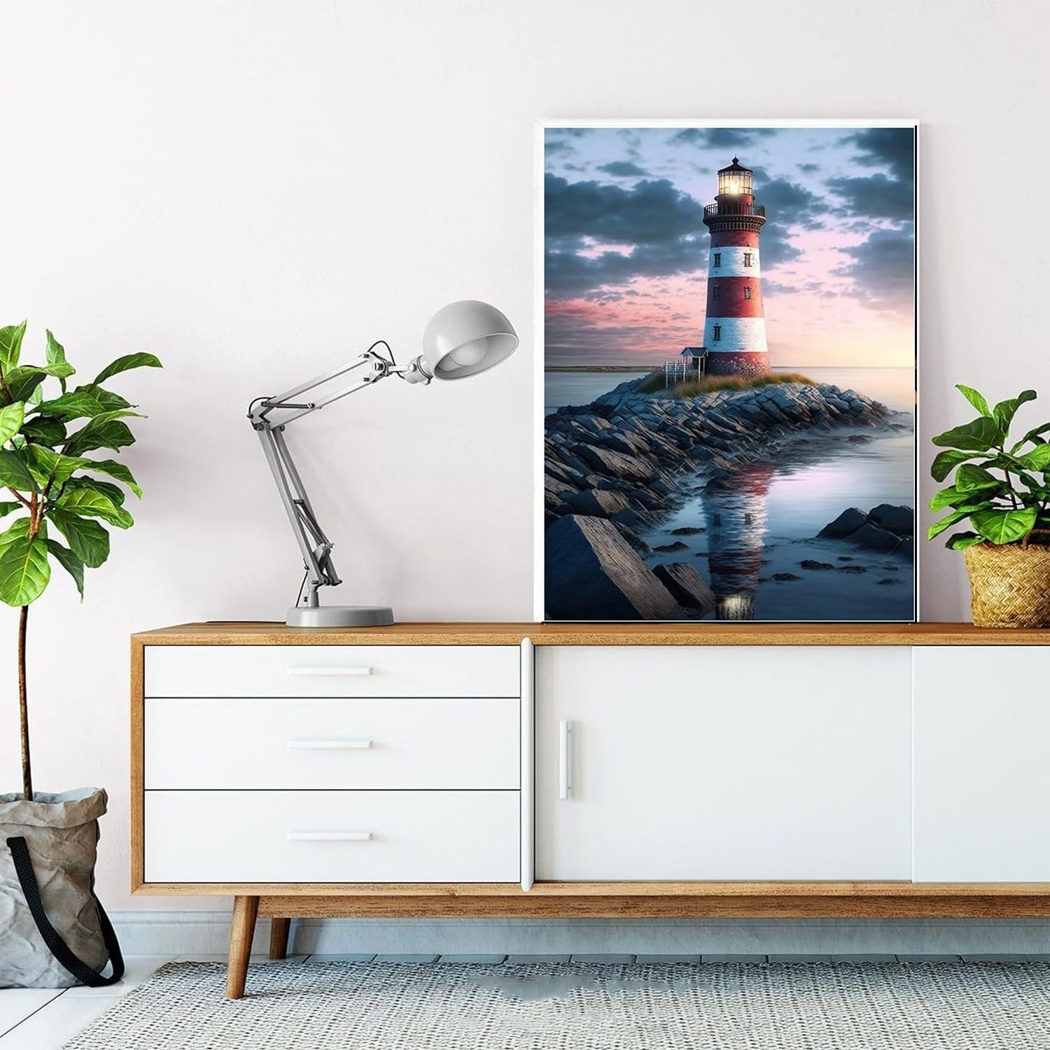 Diamond painting kit featuring a lighthouse on a rocky shore at sunset, displayed on a wall above a credenza.