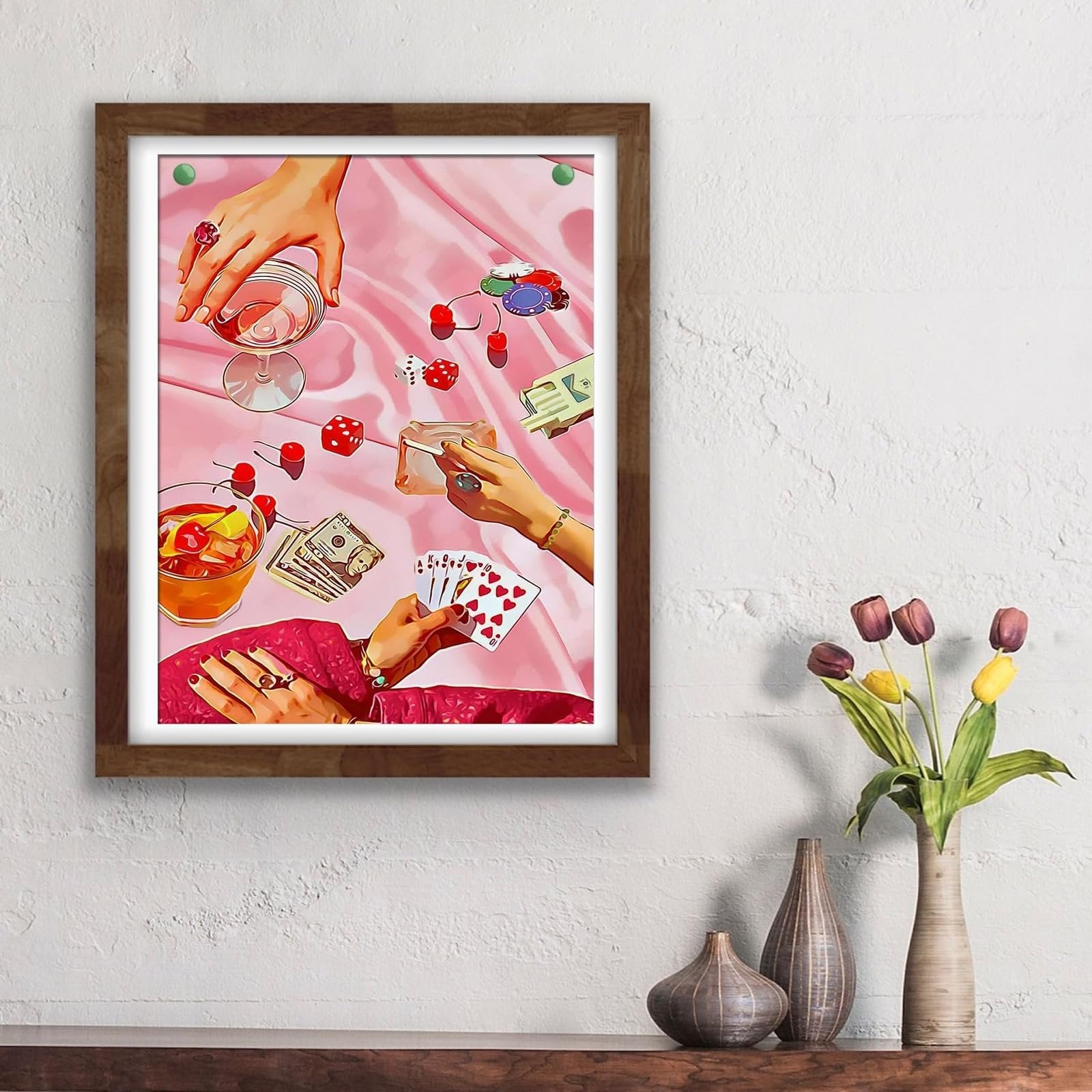 Framed artwork depicting a gambling scene with hands holding cards, dice, chips, drinks, and money on a pink satin cloth.