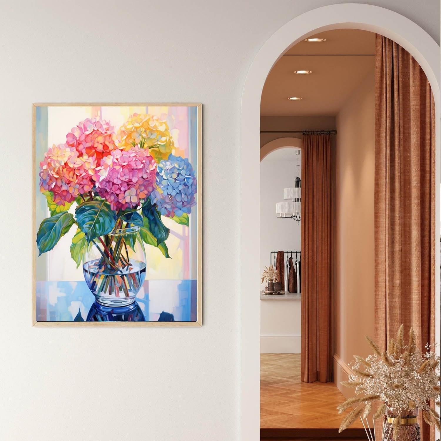 Colorful hydrangea flowers in a glass vase on a reflective surface, framed artwork on a wall.