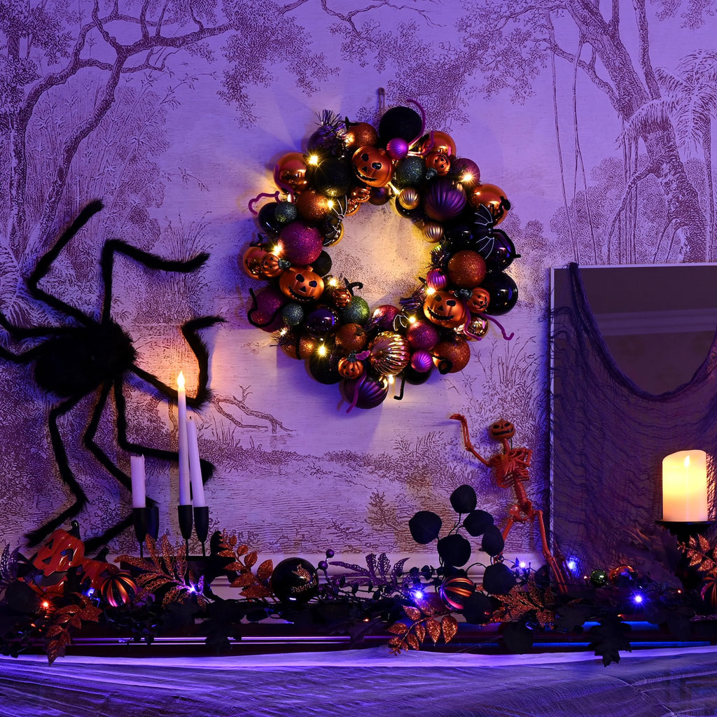 Halloween wreath with pumpkins and ornaments, lit by fairy lights, displayed above a mantelpiece with spider and candles.