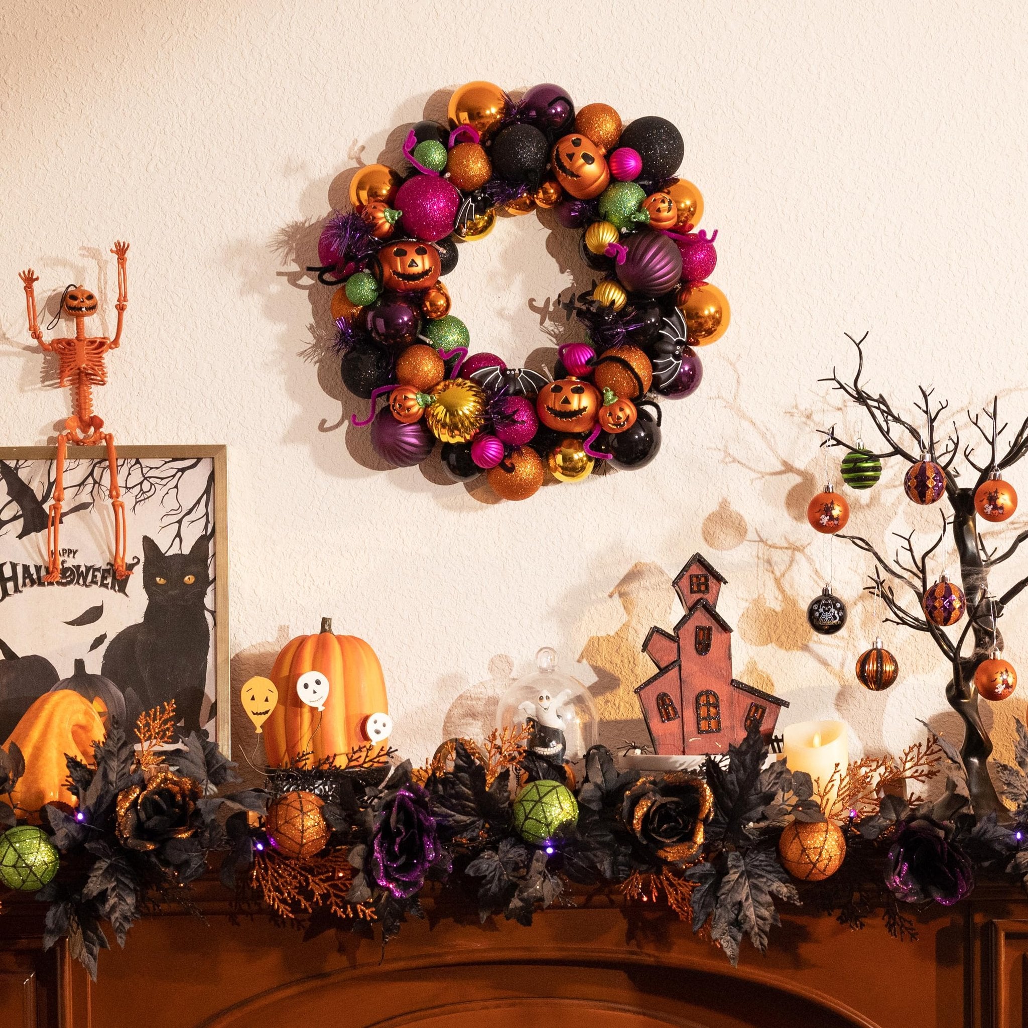 Halloween mantelpiece decor featuring a ball wreath, skeleton, framed art, pumpkins, and a decorative tree with ornaments.