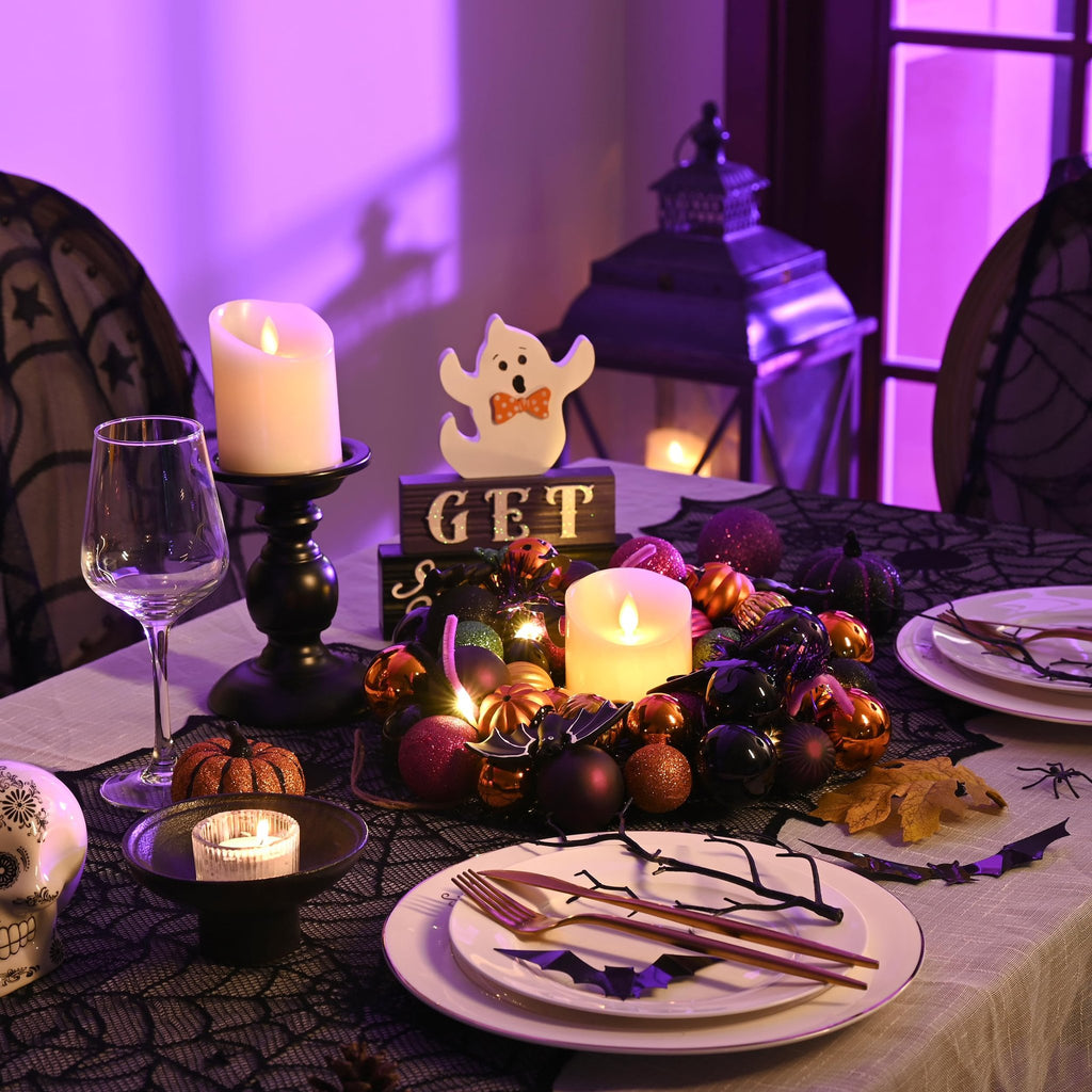 Halloween table setting with a wreath, candles, skull, and place settings under purple lighting.