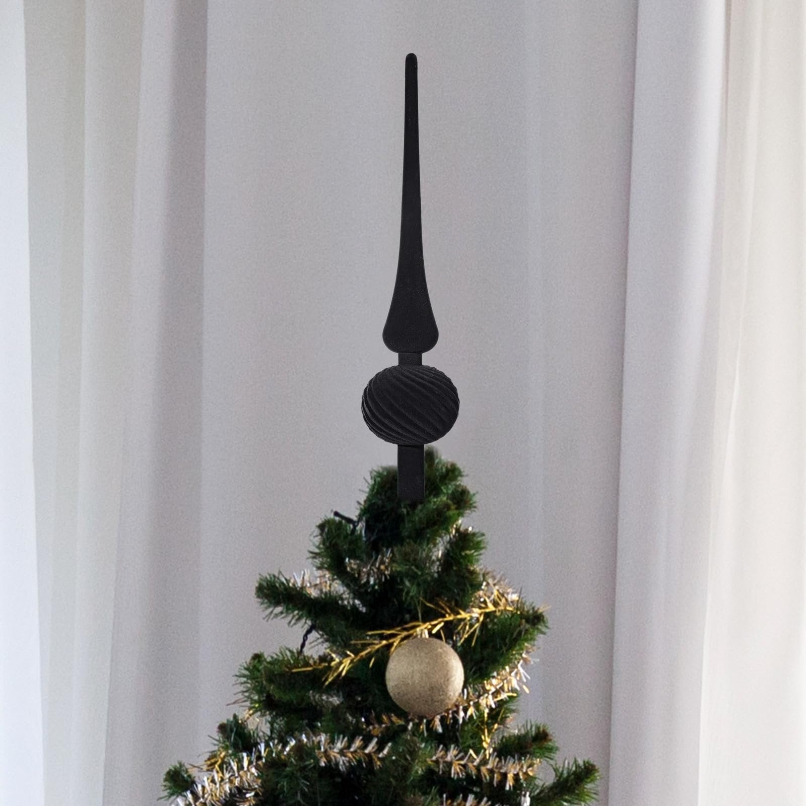 Black velvet finial Christmas tree topper with a spherical ornament on a decorated tree against a white curtain background.