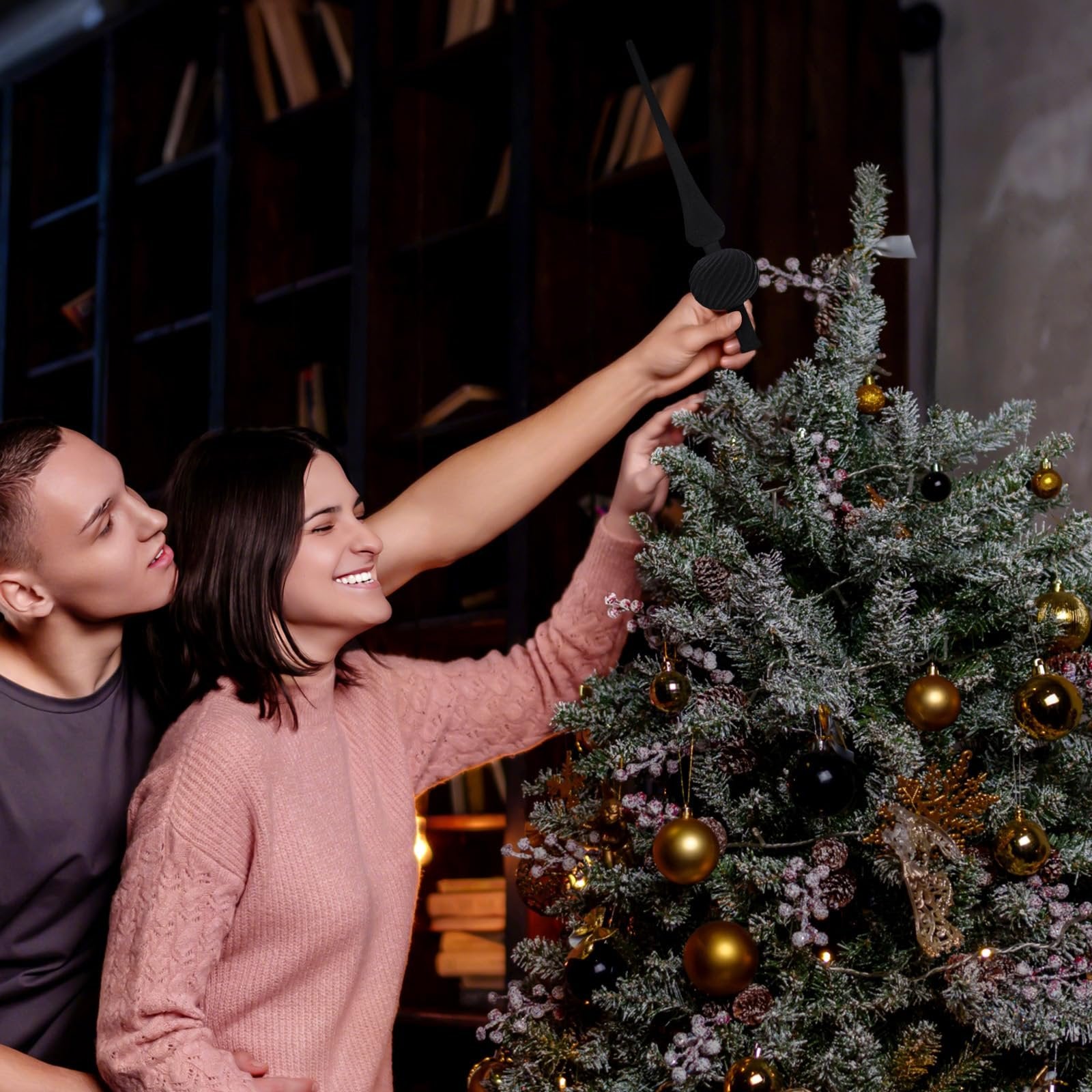 Couple decorating a Christmas tree, woman places black velvet finial topper on the tree