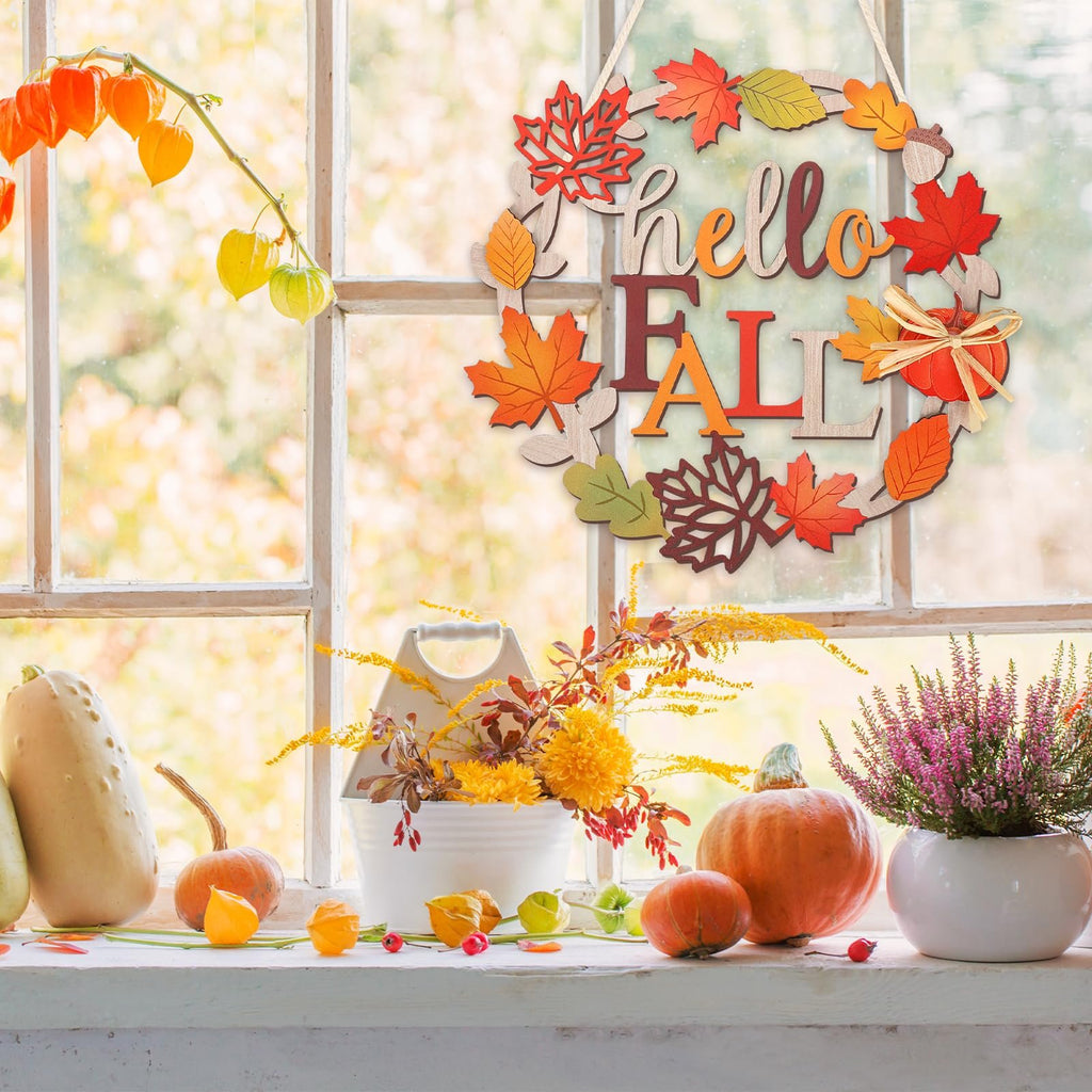 Wooden fall wreath with 'hello FALL' text and autumn leaves, displayed on a windowsill with pumpkins and flowers.