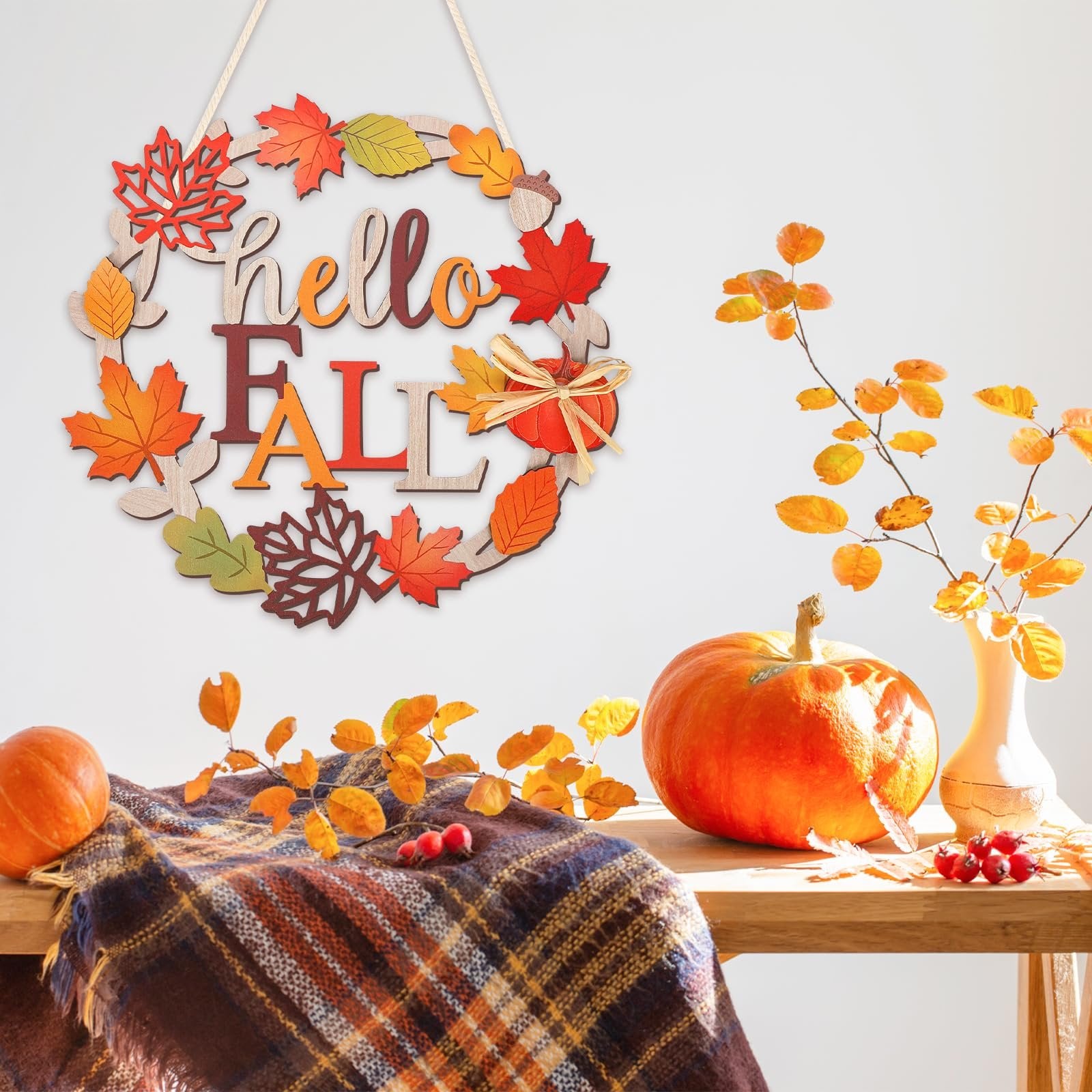 Wooden fall wreath with 'hello FALL' text, decorated with colorful leaves and a small pumpkin, displayed on a table with pumpkins and autumn branches.