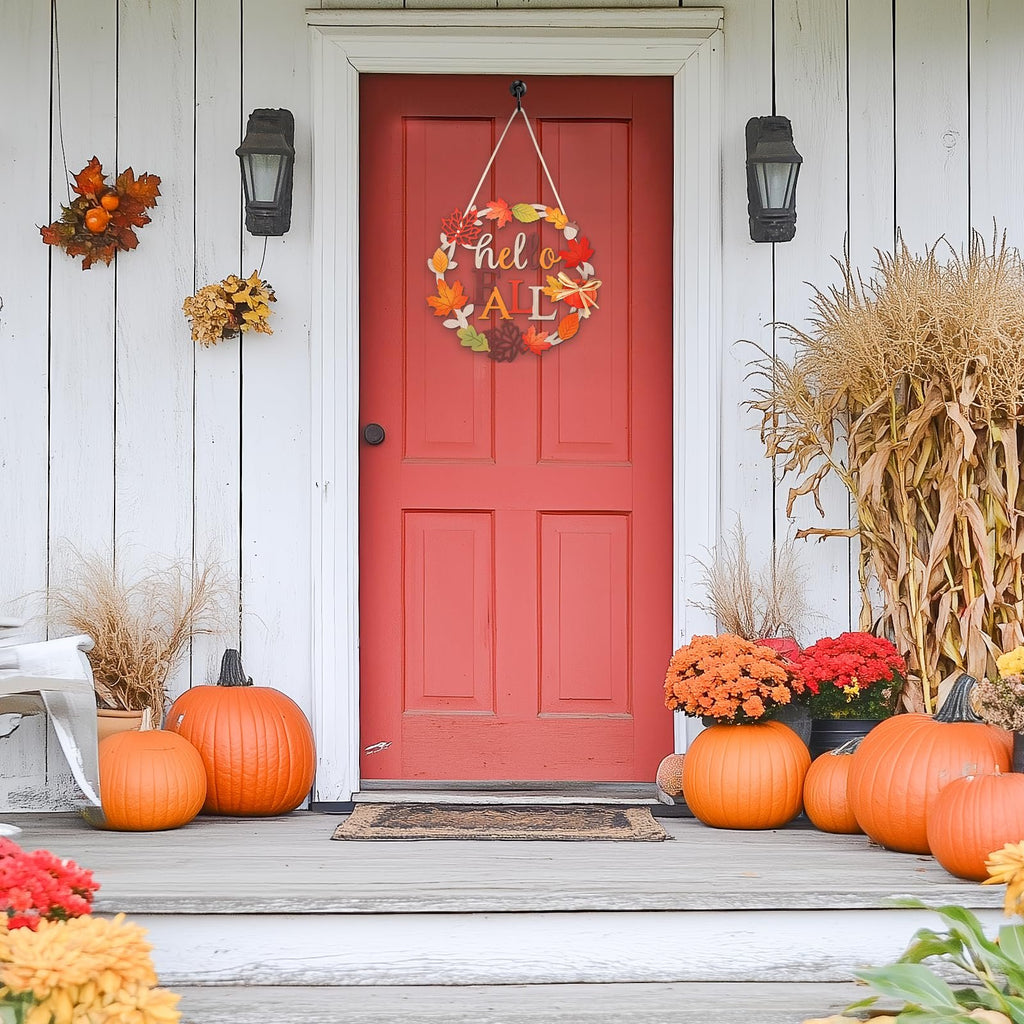 Wooden fall wreath with 'hello FALL' text hanging on a red door, surrounded by pumpkins and autumn decor.
