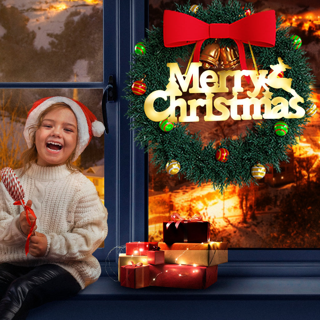 Child in Santa hat holding candy cane sits by window with Christmas wreath and gifts