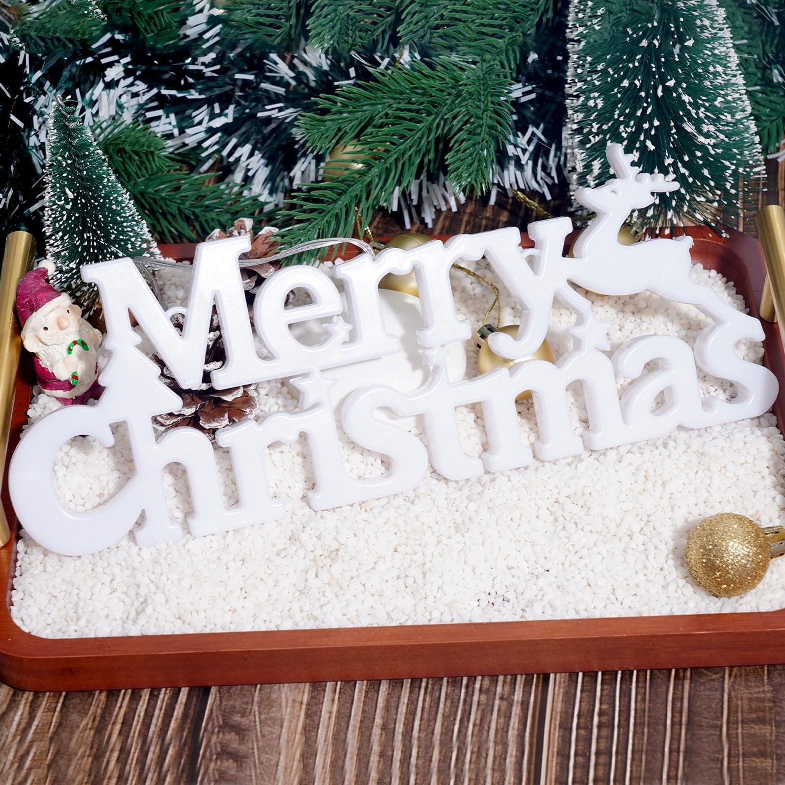 White "Merry Christmas" sign with LED lights and a reindeer, displayed on a tray with white pebbles and festive decorations.