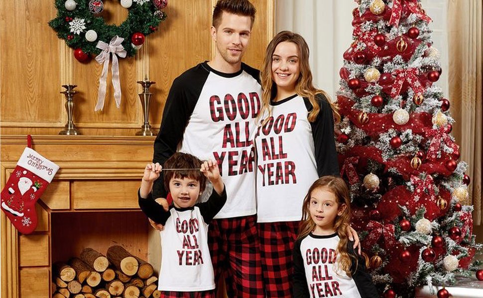 Family of four in matching Christmas pajamas posing by a fireplace and decorated tree.