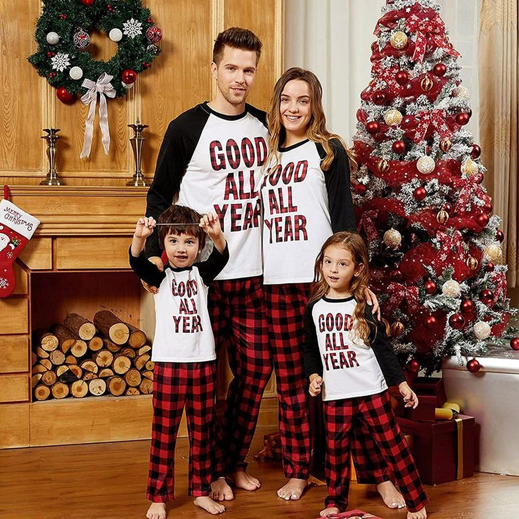 Family of four in matching Christmas pajamas posing in front of a fireplace and decorated tree.
